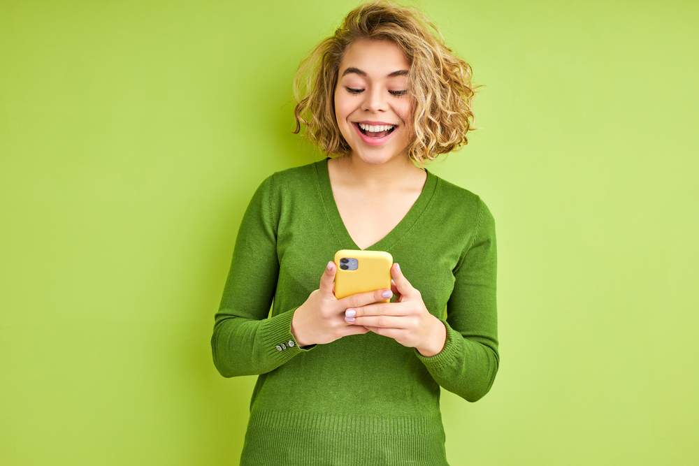 Excited,Female,Using,Smartphone,,Young,Woman,In,Green,Casual,Shirt