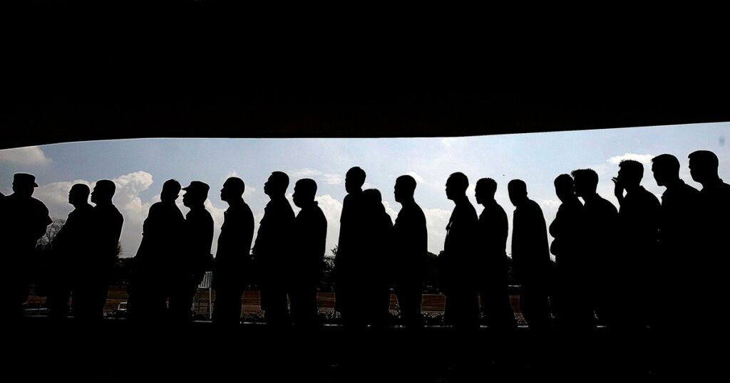 A long line of people standing one behind another, shown in full silhouette against a bright cloudy sky, framed by dark bands above and below.